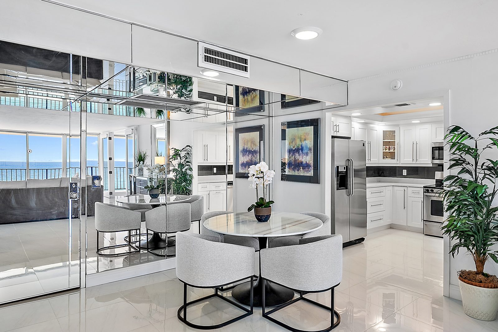 Mirrored dining nook with marble round table and modern sculpted chairs, adjacent to kitchen and oceanfront living room