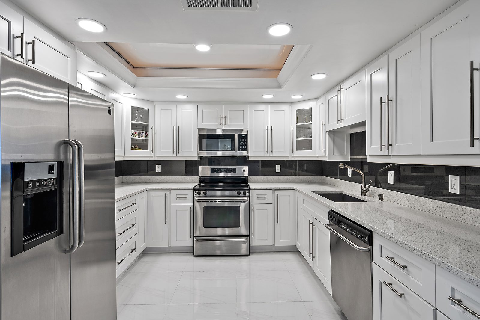 Renovated white kitchen with stainless steel appliances, recessed lighting, and granite accents