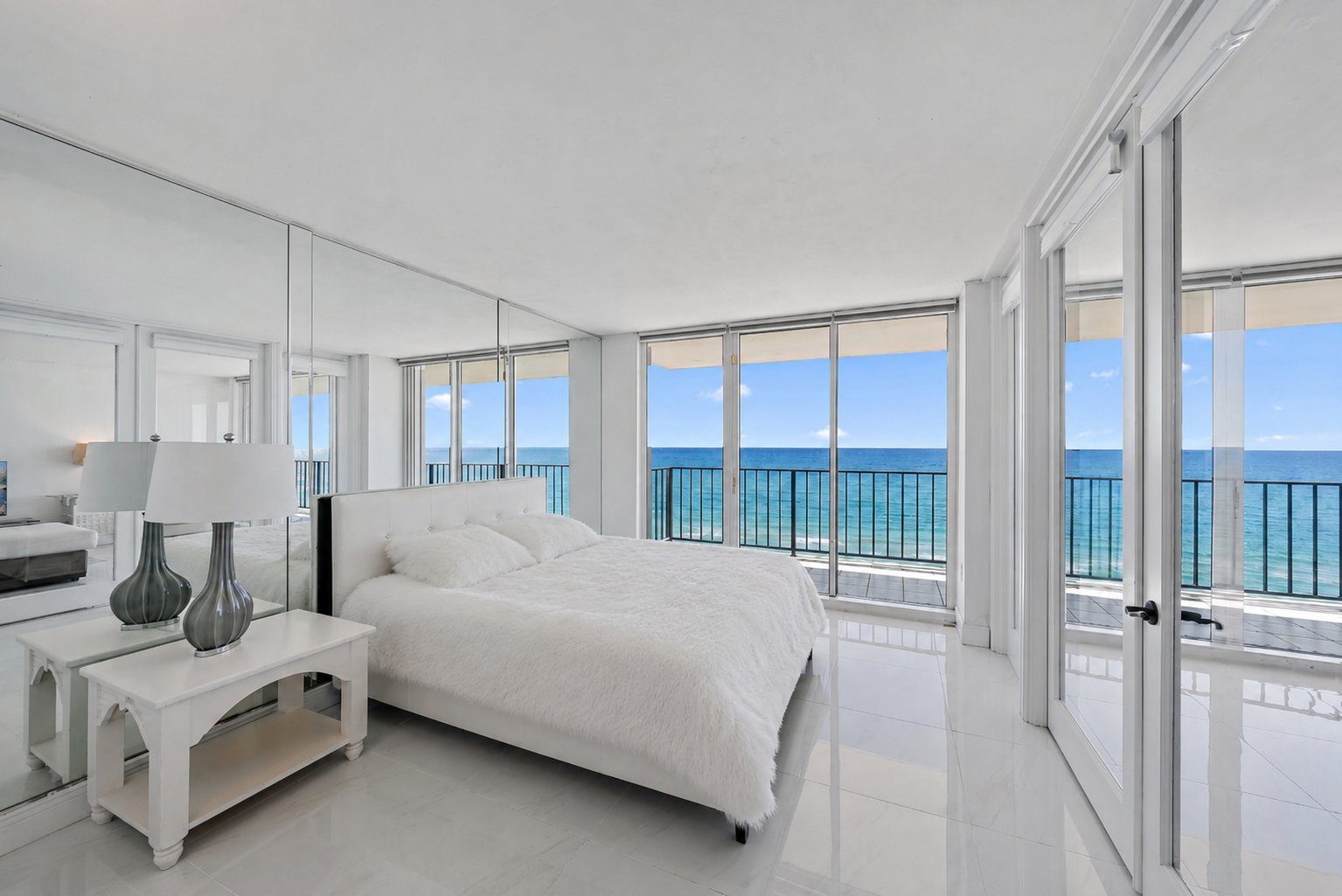 Master bedroom with floor-to-ceiling glass overlooking the Atlantic, mirrored wall, and direct terrace access