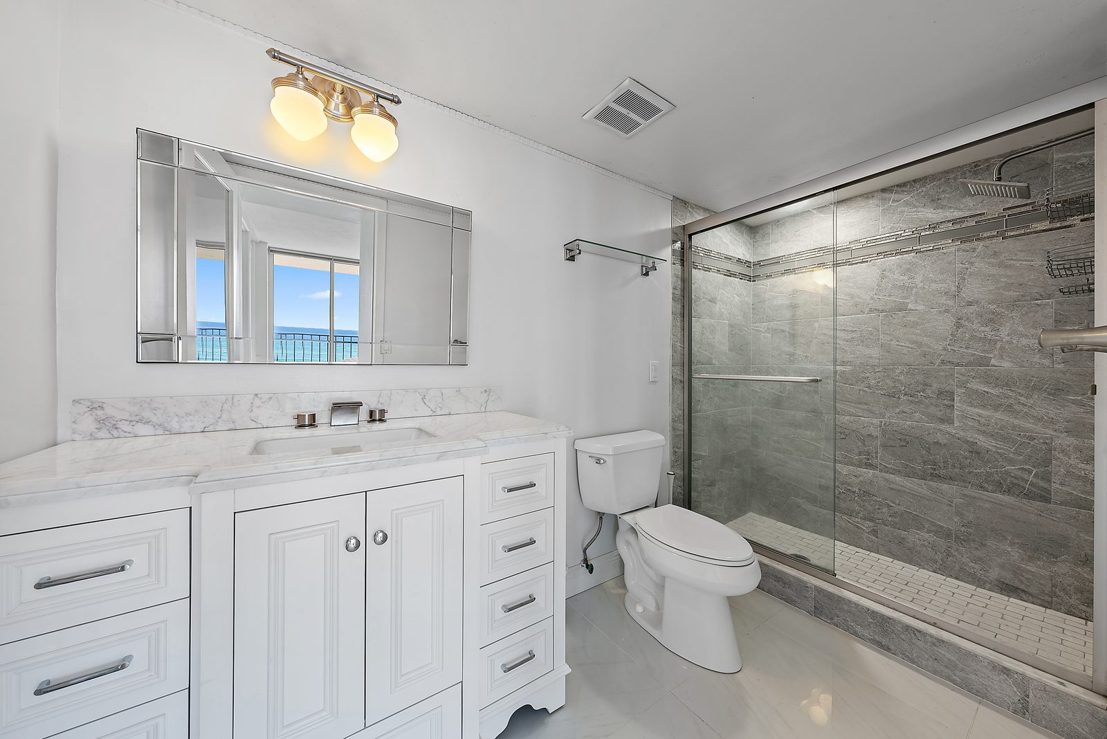 Primary bathroom with marble countertop, large glass shower, and ocean view reflected in the mirror